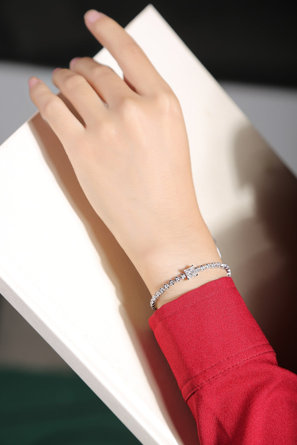 Hand wearing a silver bracelet on a white surface