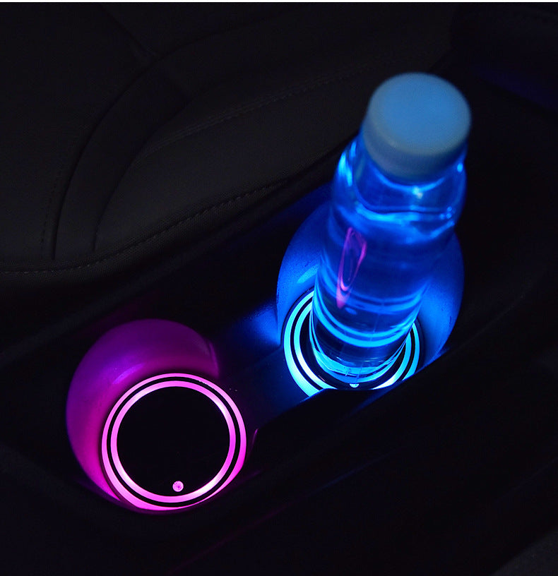 Car cup holder with glowing pink and blue coasters and a water bottle.