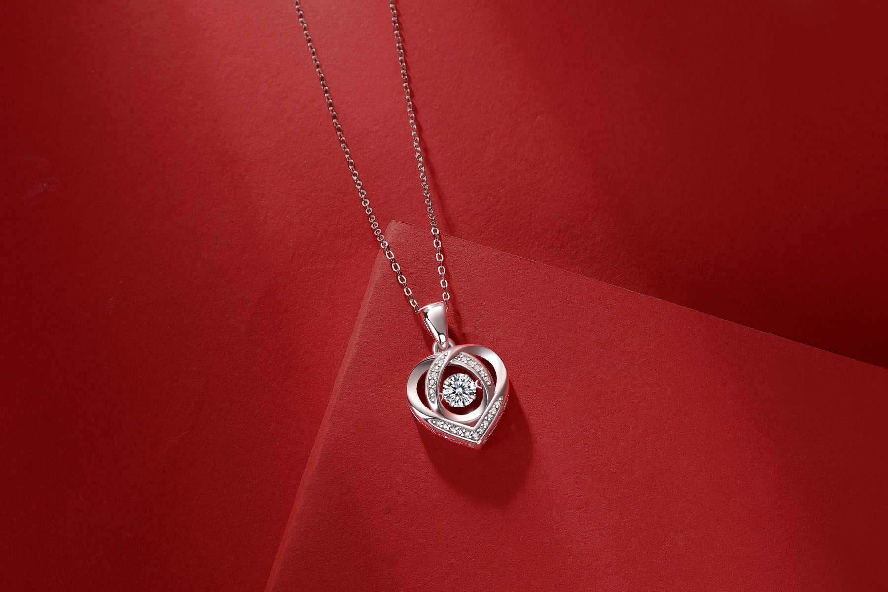 Silver heart-shaped pendant with clear stones on a red background